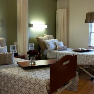 A well-decorated hospital room with two beds, pillows, tray tables, and calming lighting.