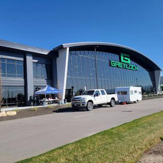 A modern commercial building featuring large glass windows and a prominent logo, with vehicles parked outside under a clear blue sky.