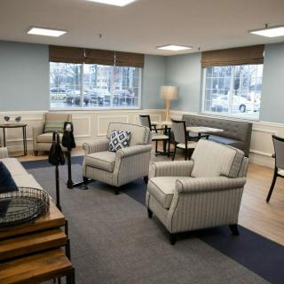 A cozy living room with chairs, a sofa, and a table, featuring large windows and a standing lamp.