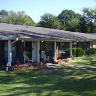 A suburban house with a porch and well-maintained lawn surrounded by trees.