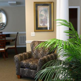 A cozy living area featuring a patterned armchair, decorative plant, and framed artwork near a dining space.