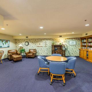 A cozy lounge area featuring comfortable chairs, a central table, and bookshelves on a carpeted floor.