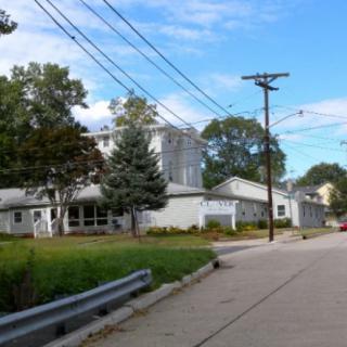 A suburban street view featuring a building, trees, and power lines under a clear sky.