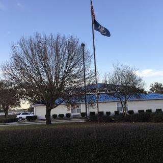 A building with a flag flying in front, surrounded by trees and a clear sky.