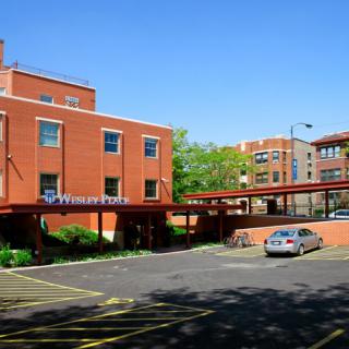 A view of a brick building with an adjacent parking lot featuring a single parked car on a sunny day.