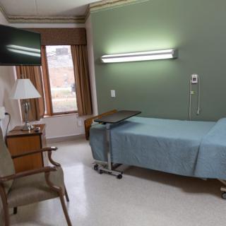 A hospital room with a single bed, television, chair, and window with curtains.