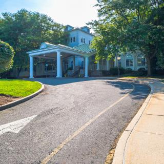 A sunlit building with a driveway and tree-lined entrance.