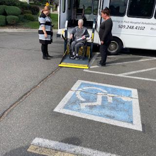 A scene depicting two individuals assisting a person in a wheelchair onto a bus equipped with a ramp.