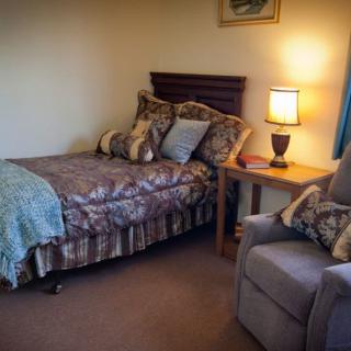 A cozy bedroom with a single bed, nightstand with a lamp, and a comfortable chair.