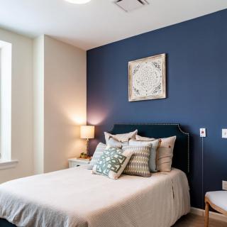 A cozy bedroom with a stylish blue accent wall, featuring a neatly made bed adorned with decorative pillows and soft lighting from a bedside lamp.