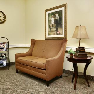 A cozy waiting room with a brown sofa, side table, and decorative lamp.
