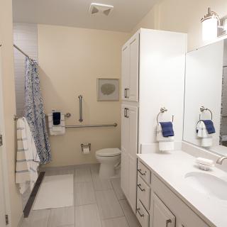 A clean and accessible bathroom with a sink, mirror, toilet, and shower.