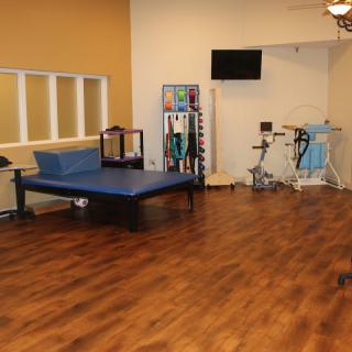 A physical therapy room equipped with exercise machines and a treatment bed on a wooden floor.