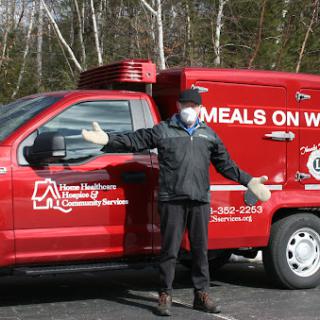 A volunteer standing beside a Meals on Wheels vehicle, promoting community support and meal delivery services.