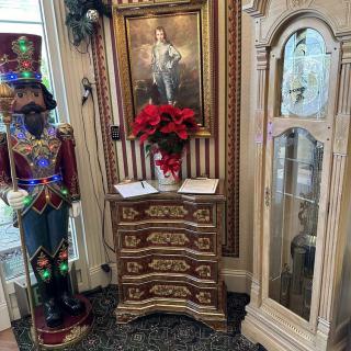 A vintage-themed interior with an ornate cabinet, festive poinsettia, and a decorative soldier figurine beside a framed painting.