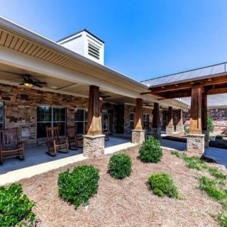 A rustic-style building with a stone facade and wooden pillars, featuring a landscaped area with shrubs.