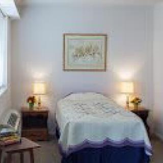 A cozy bedroom with a single bed, flanked by nightstands and lamps, adorned with a decorative painting on the wall.