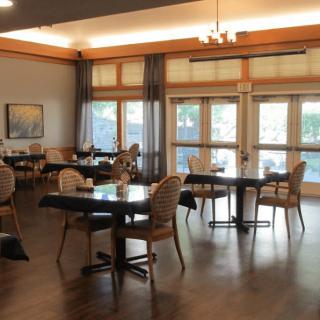An empty dining area with tables and chairs arranged neatly, featuring large windows and decor.