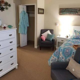 A cozy bedroom with a neatly arranged bed, armchair, dresser, and open closet.