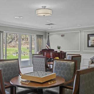 A well-furnished living room with a game table and comfortable seating, overlooking a garden view through large windows.