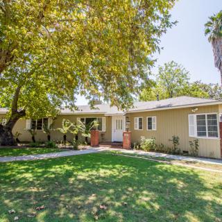 A single-story suburban house with a well-maintained yard and large trees.