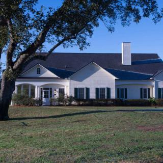 A spacious white house with a dark roof and chimney, surrounded by a grassy lawn and a large tree in the foreground.