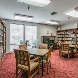 A cozy library room with tables, chairs, and bookshelves filled with books.