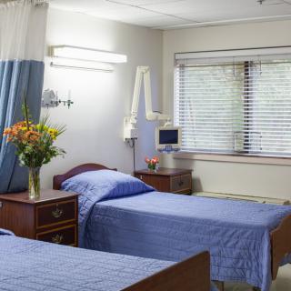 A clean and well-organized hospital room with two beds, bedside tables, and a vase of flowers near the window.