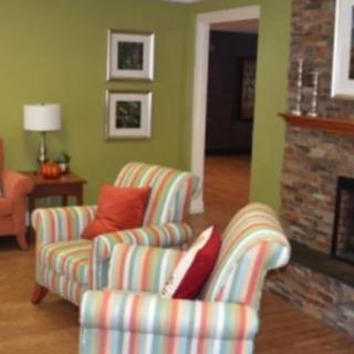 A cozy living room featuring striped armchairs, a stone fireplace, and a green accent wall.