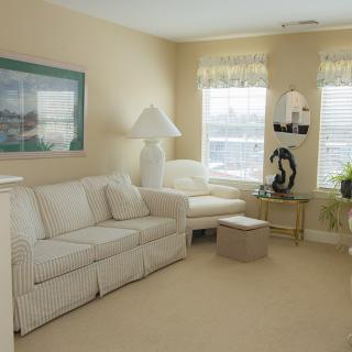 A cozy living room featuring a white sofa, table lamp, and decorative elements with large windows providing natural light.
