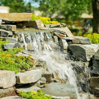 A serene garden waterfall cascading over rocks surrounded by lush greenery.
