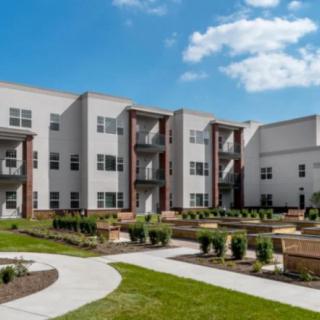 A modern apartment complex with well-maintained landscaping under a clear blue sky.