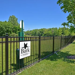 A fenced dog park with lush green surroundings and a clear blue sky.