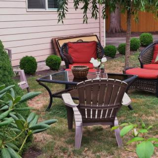 A cozy backyard setup featuring patio furniture with red cushions, a glass coffee table, and surrounding greenery.