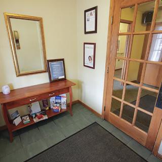 A cozy entryway with a wooden table, mirror, certificates on the wall, and a glass-paneled door.