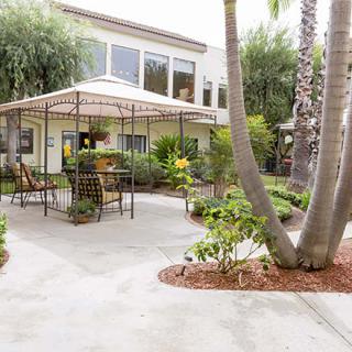 A peaceful garden patio with a gazebo and seating area surrounded by lush greenery.