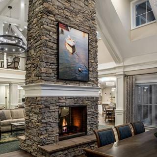 A luxurious open-concept living and dining area featuring a central stone fireplace with artwork above it.