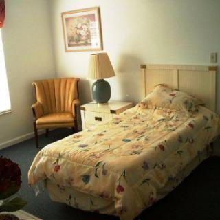 A cozy bedroom with a single bed, nightstand, lamp, chair, and wall art.