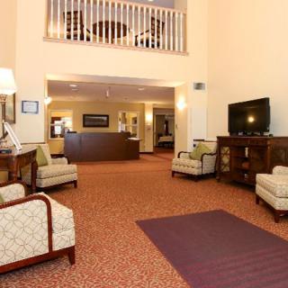 A spacious hotel lobby with comfortable seating, a television, and a reception desk in the background.