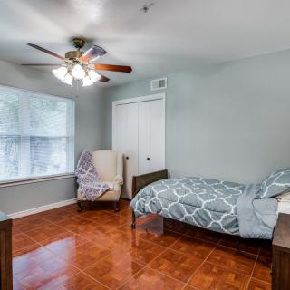 A cozy bedroom with a single bed, armchair, and ceiling fan.