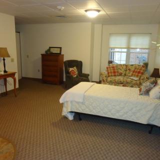 A spacious bedroom with a bed, sofa, chest of drawers, and chair.