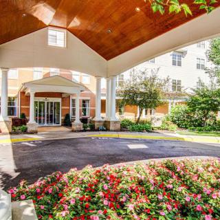 A beautifully landscaped building entrance with a covered walkway and vibrant flower beds.
