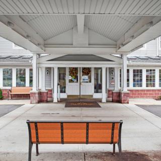 A building entrance with a covered walkway and an orange bench in the foreground.