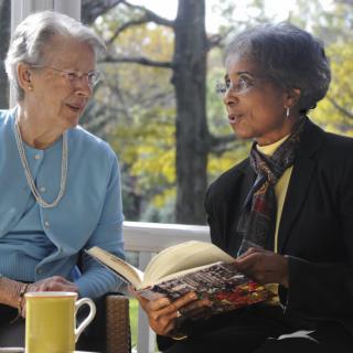 Two elderly women engaged in a conversation while reading a book indoors.