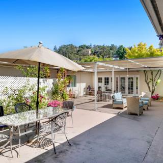 A spacious outdoor patio with comfortable seating, umbrellas, and a garden backdrop on a sunny day.