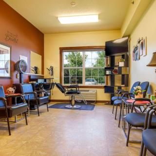 A well-lit waiting room with chairs arranged around a central area, featuring a large window and a television.