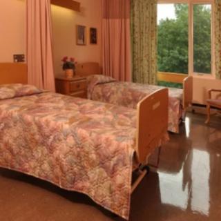 A hospital room with two beds, chairs, and a window.