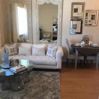 A cozy living room with a plush sofa, decorative pillows, and a glass coffee table, adjacent to a small dining area.