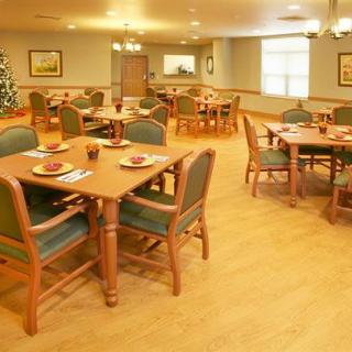 A cozy dining area with several tables and chairs arranged neatly, featuring warm lighting and wooden flooring.