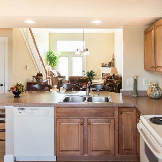 A modern kitchen with wood cabinetry opens into a bright living area.